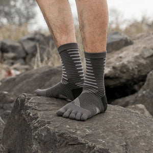 Person standing on a rock wearing grey striped five-toe socks, in an outdoor setting.