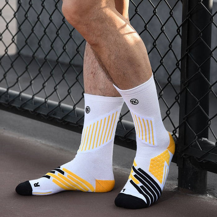 Athlete leaning against a fence wearing white socks with yellow design elements and black accents.