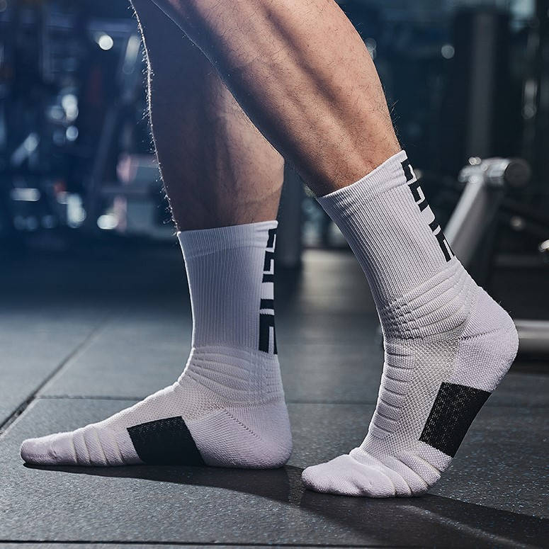 Athlete wearing white sports socks with black heel patches, standing in a gym with equipment in the background.