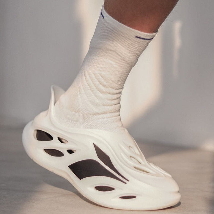 Close-up of a foot in a white futuristic sneaker with cut-out details, paired with a white sock with a blue stripe.