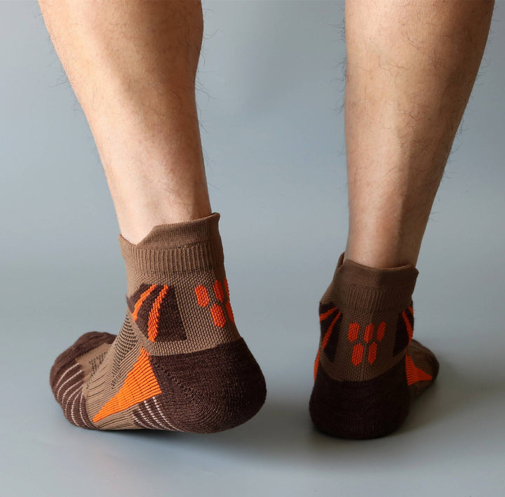 Person wearing brown ankle socks with orange pattern and non-slip grips on the heel.