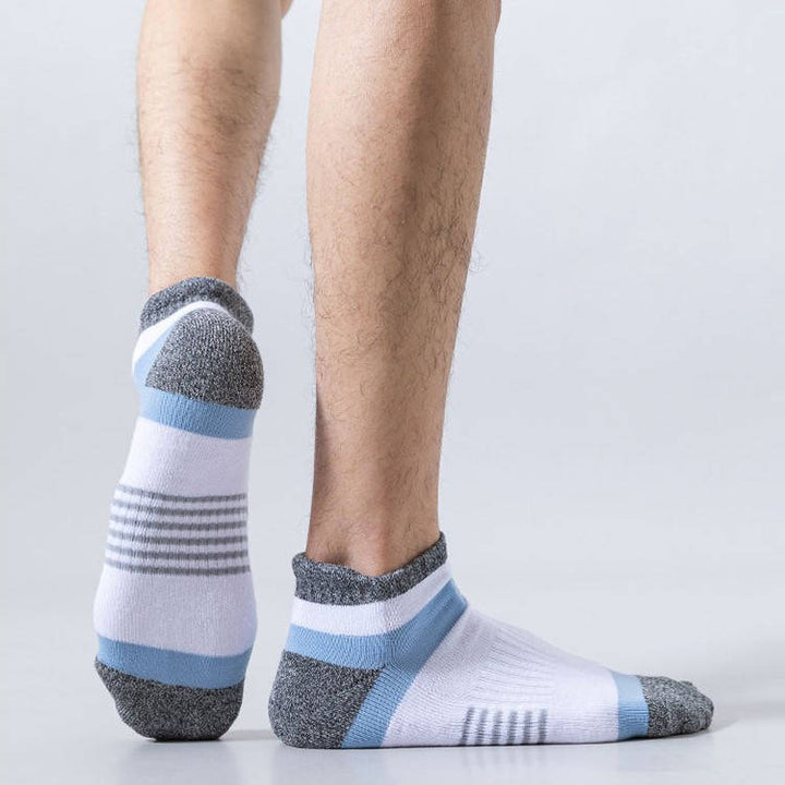 A person standing in white sports socks with blue stripes and grey reinforced heel and toe areas.