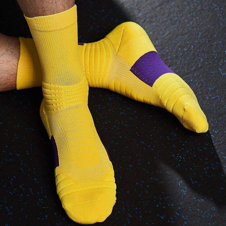 Feet clad in yellow sports socks with purple bands on the arches, resting on a speckled gym floor.